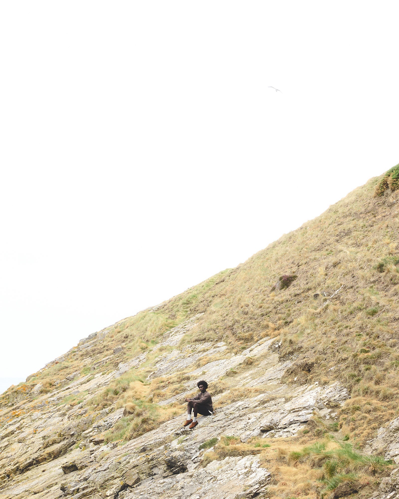 Wide landscape shot of a man sat on a steep grass and rock hillside above the Aberdeenshire coast