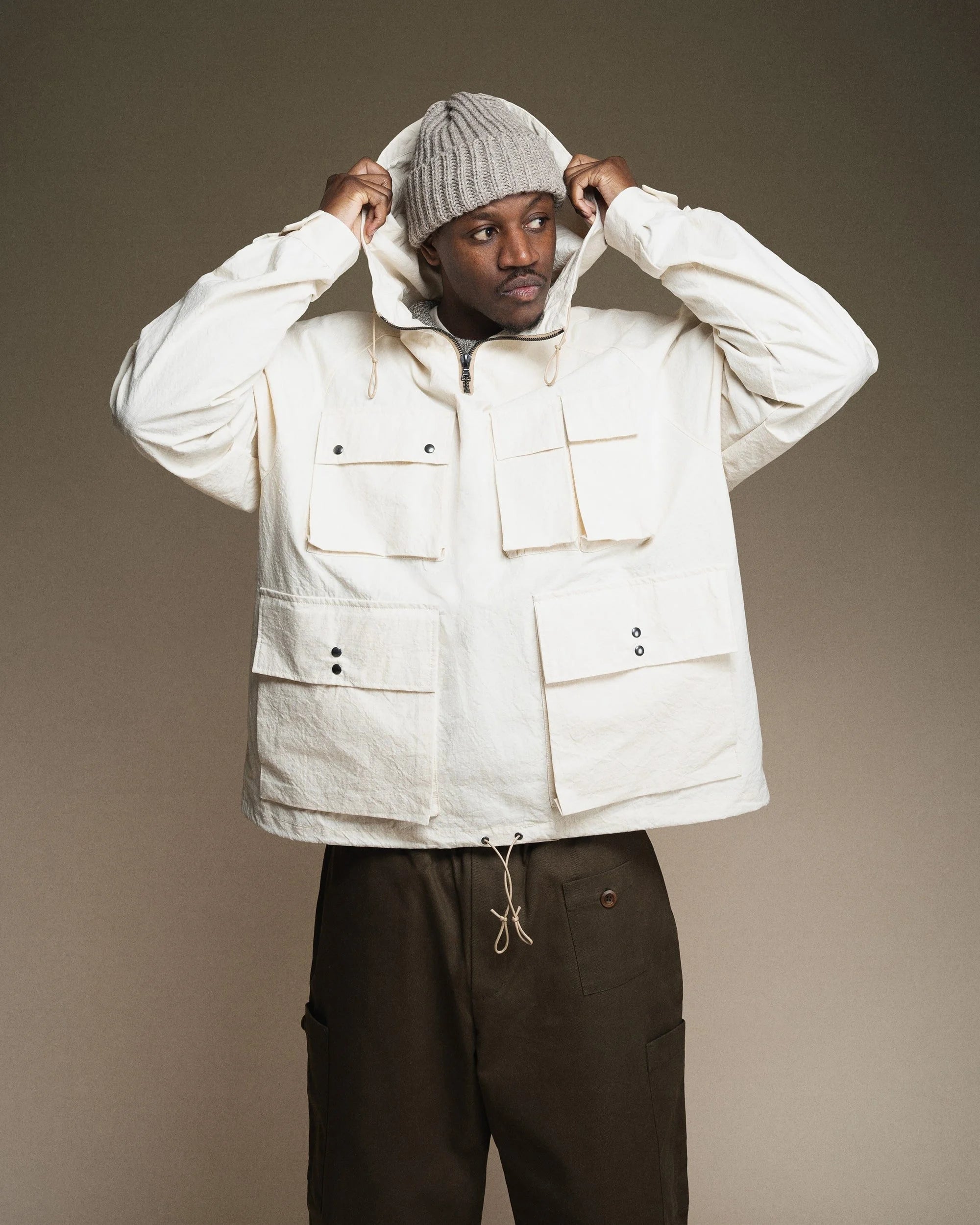 Person wearing a white jacket and brown pants against a plain background